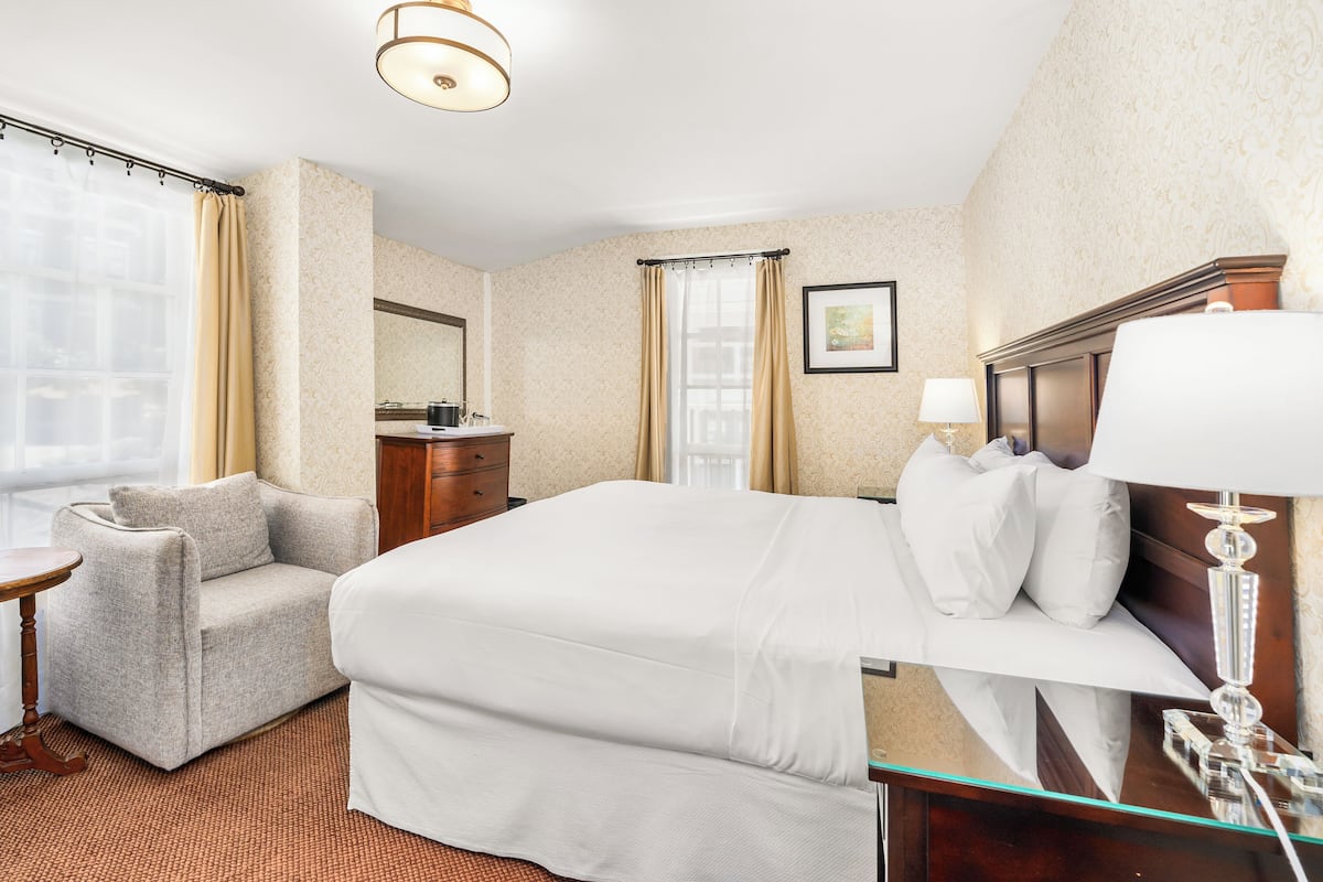 A hotel room with a large bed, a chair, a dresser, a mirror, and a window with curtains.