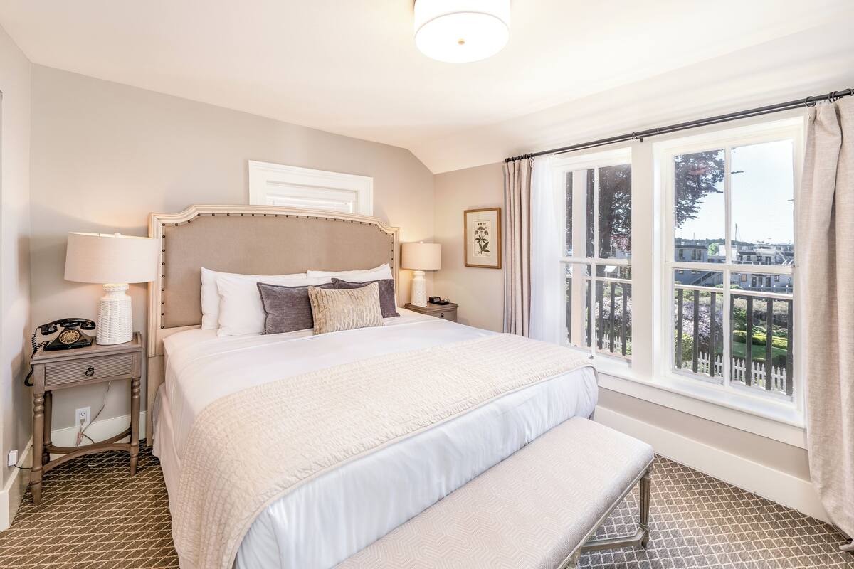 A neatly arranged hotel room with a large bed, bedside lamps, a telephone, and a window with a view of the outside.
