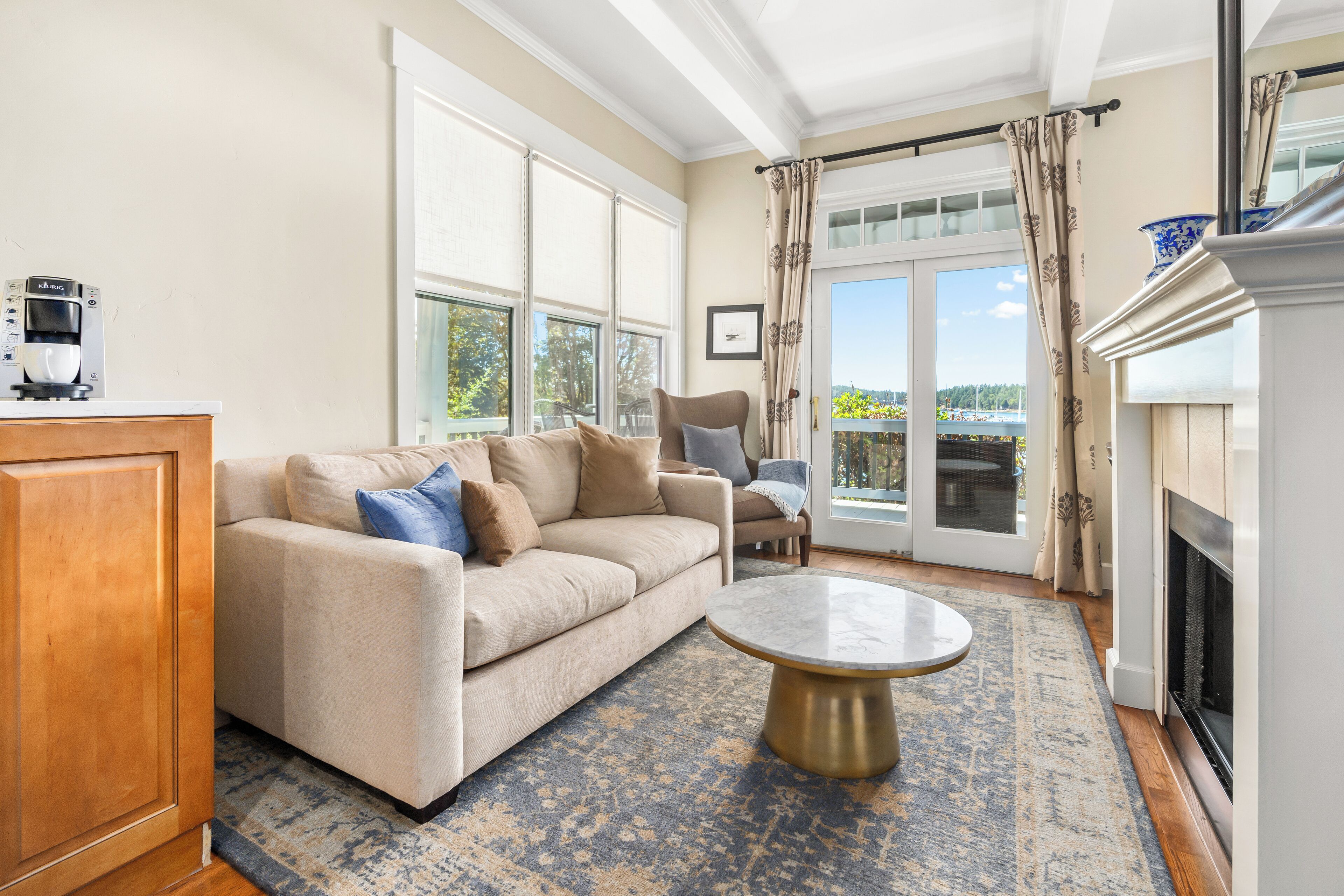 Una sala de estar con sofá, sillón, cafetera, chimenea y ventanas amplias.