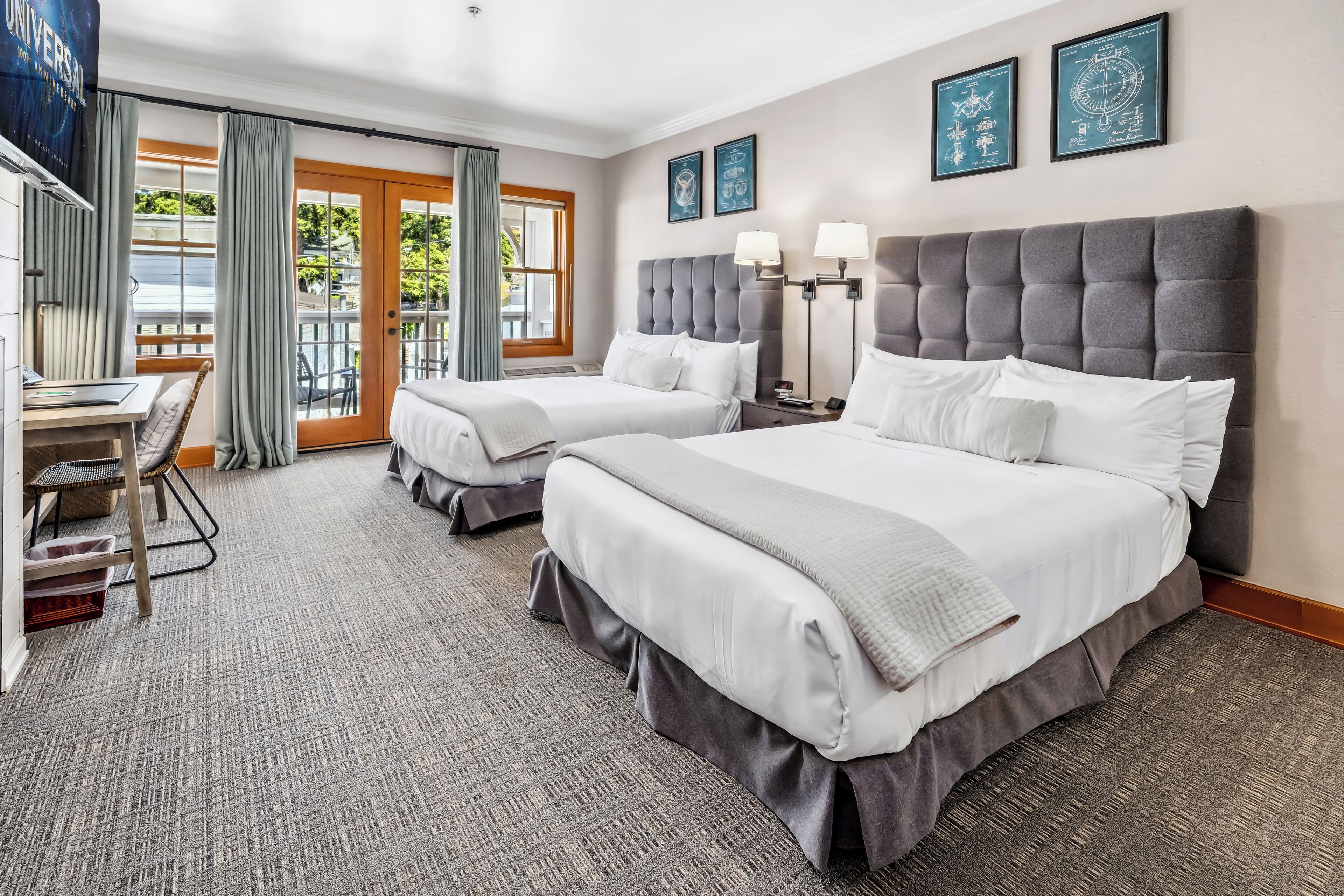 A hotel room with two beds, a desk, and a view of the outdoors.