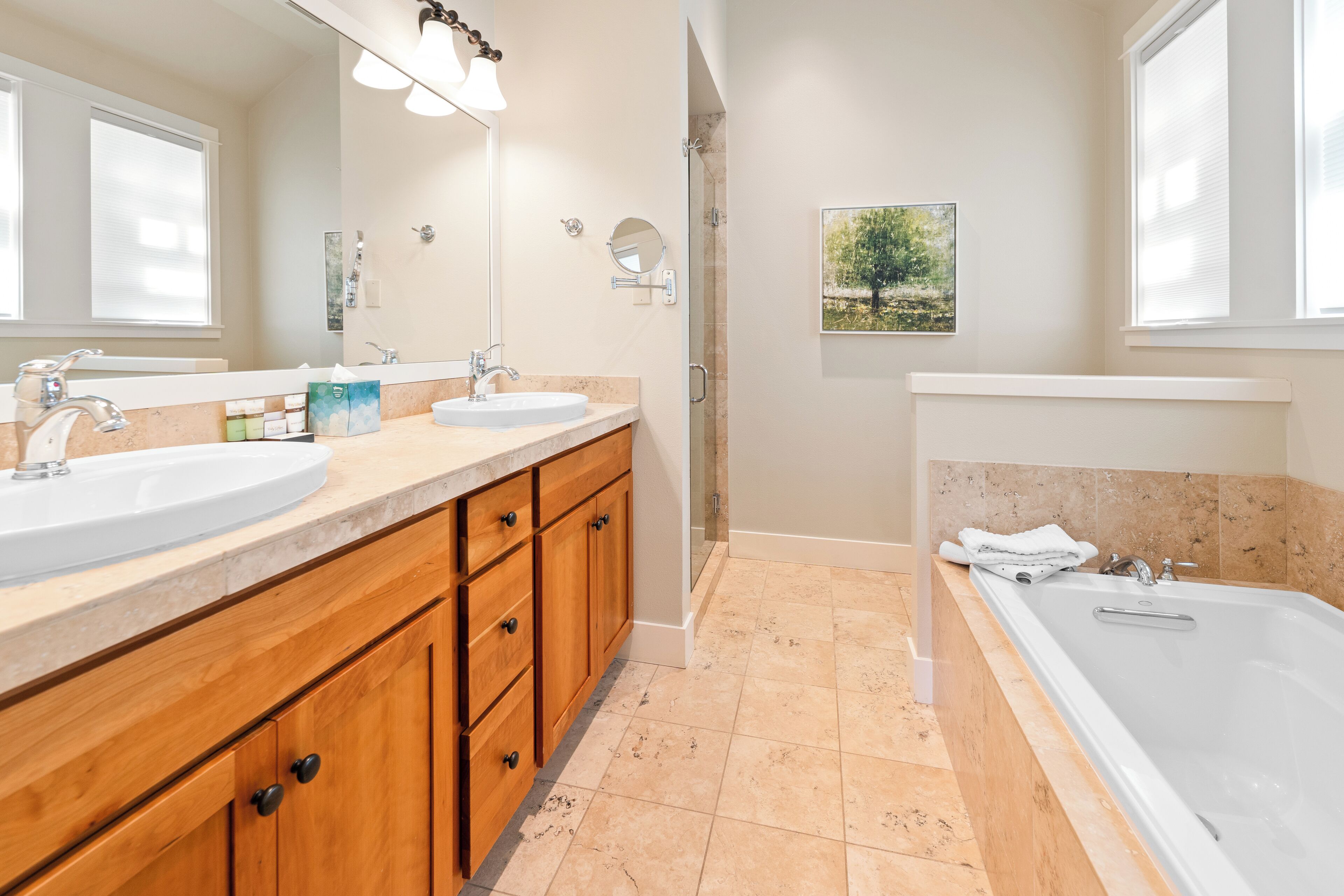 A modern bathroom with two sinks, a bathtub, wooden cabinets, and a large mirror.