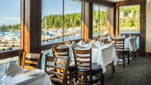 A restaurant with tables set for dining, large windows offering a view of boats and greenery. - Roche Harbor Resort (Friday Harbor)