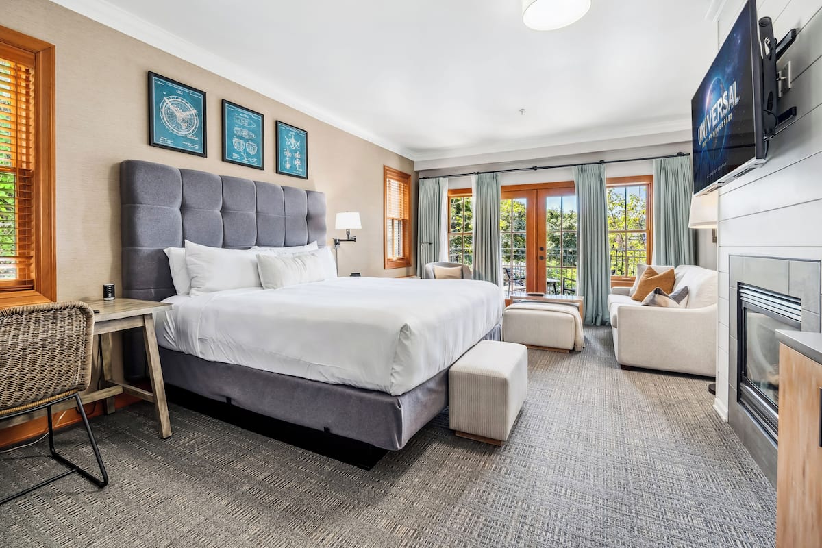 A hotel room with a large bed, a desk, a chair, a sofa, a television, and a fireplace.