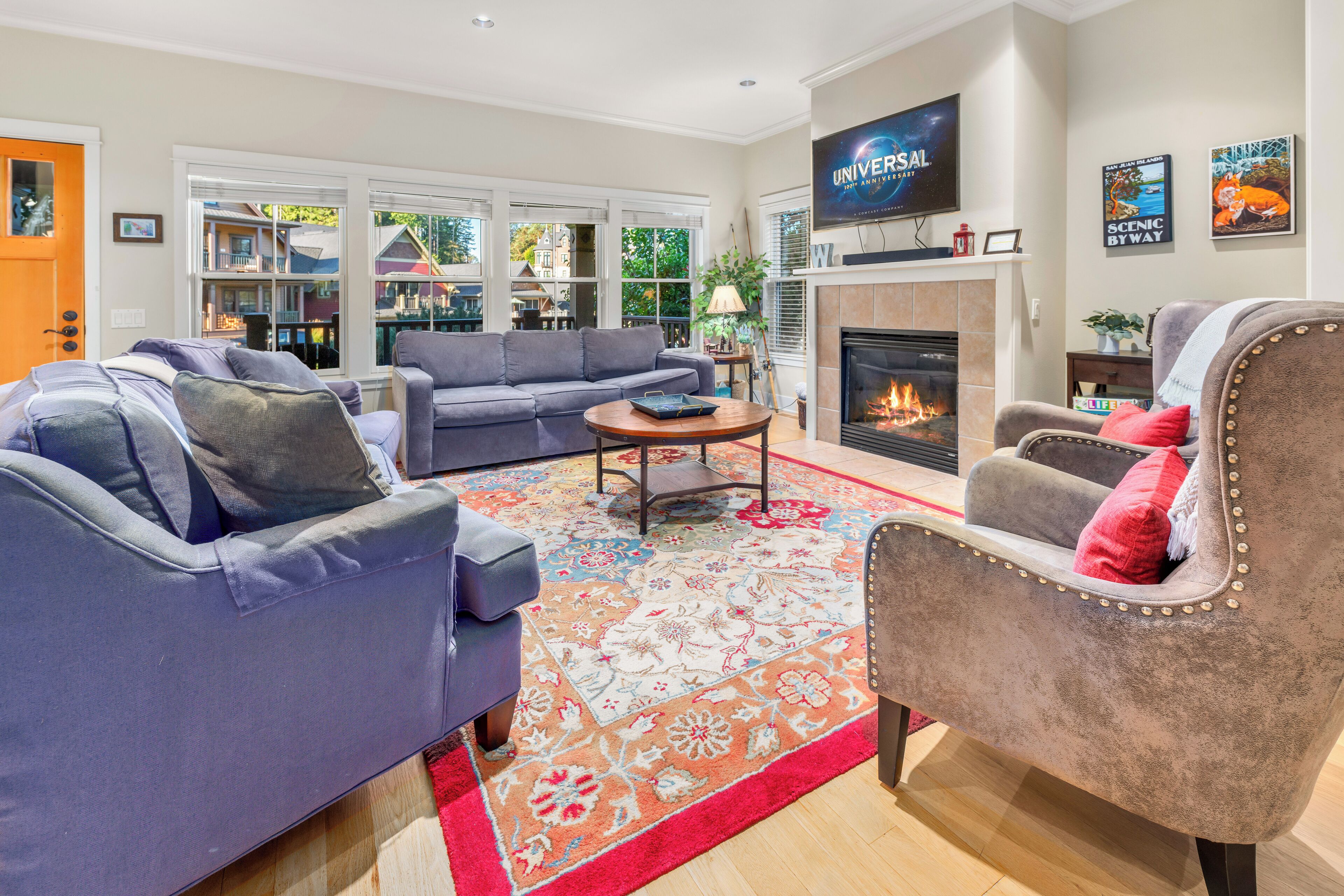 A living room with a fireplace, a television mounted above it, and a large window with a view of the outside.
