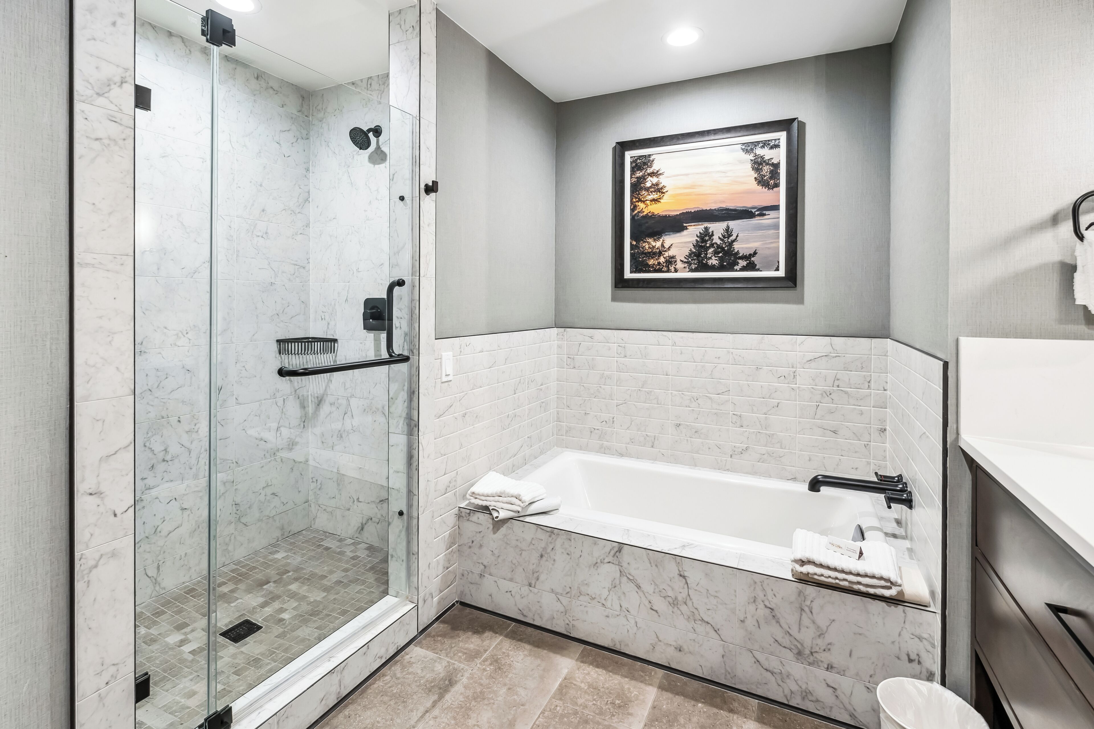 Un bagno moderno con cabina doccia in vetro, una vasca da bagno bianca e un quadro appeso alla parete.