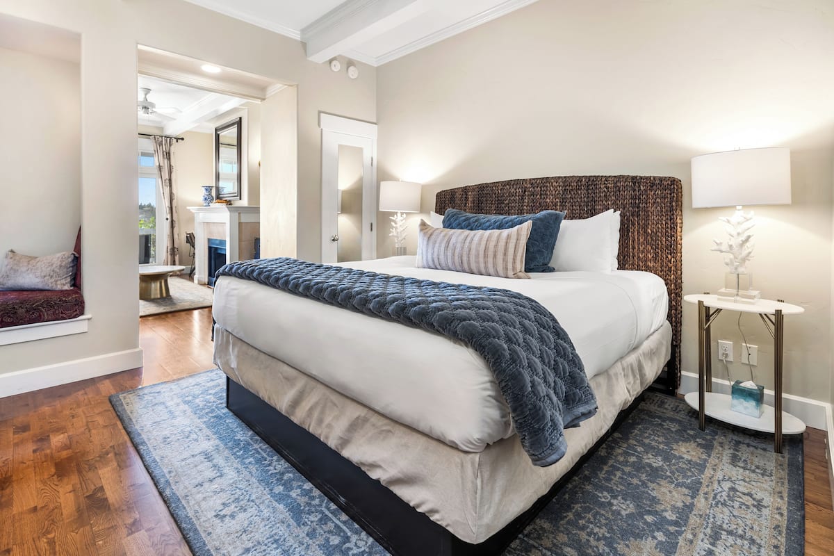 A modern bedroom with a large bed, a bedside table with a lamp, and a view of a hallway.