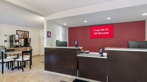Un espace d’accueil d’hôtel avec un mur rouge, un panneau indiquant « Wi-Fi gratuit dans toutes les chambres », une machine à café et un coin salon avec des chaises et une table.