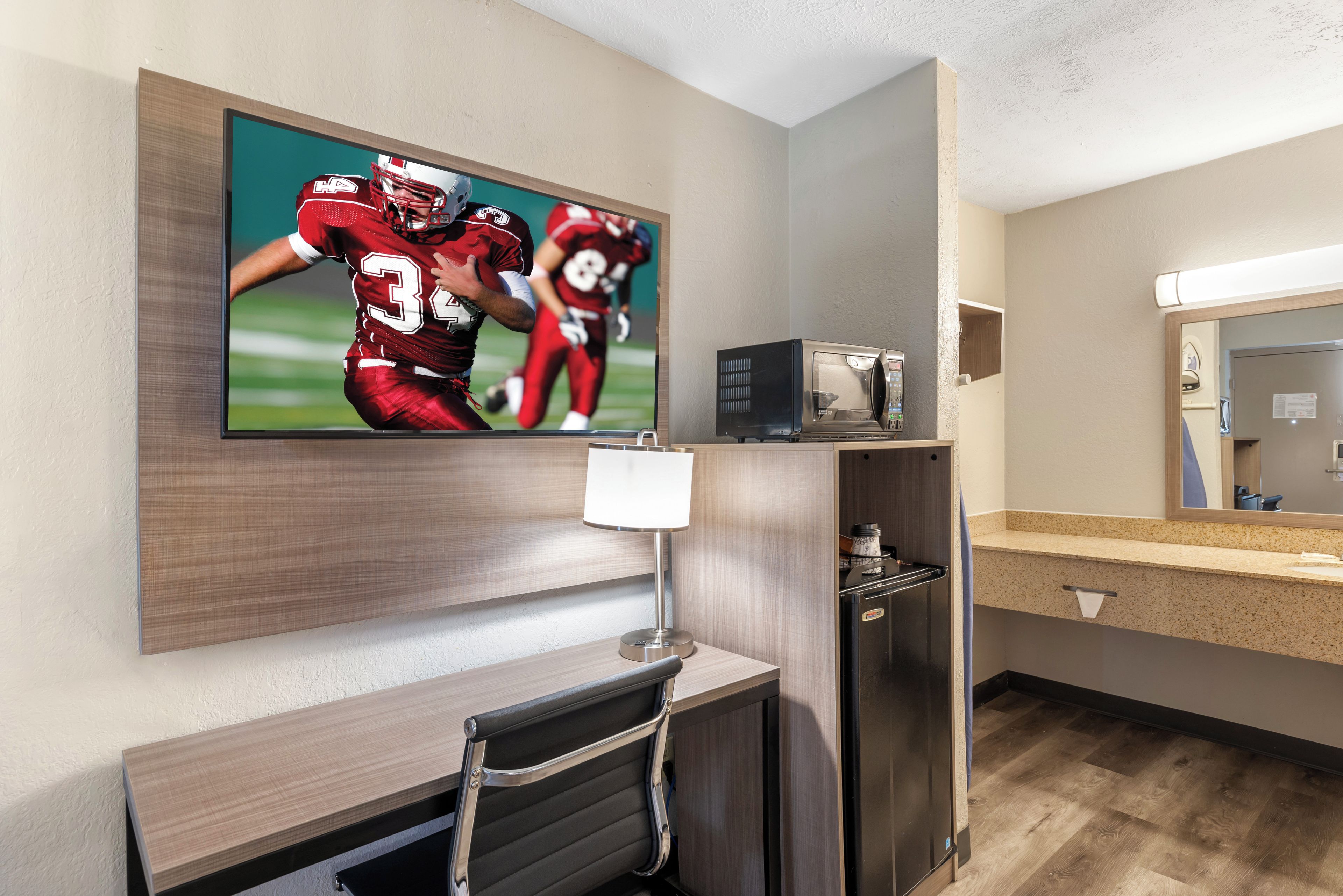 Hotelværelse med et fladskærms-tv på væggen, en mikrobølgeovn på bordet, et lille bord og en stol.