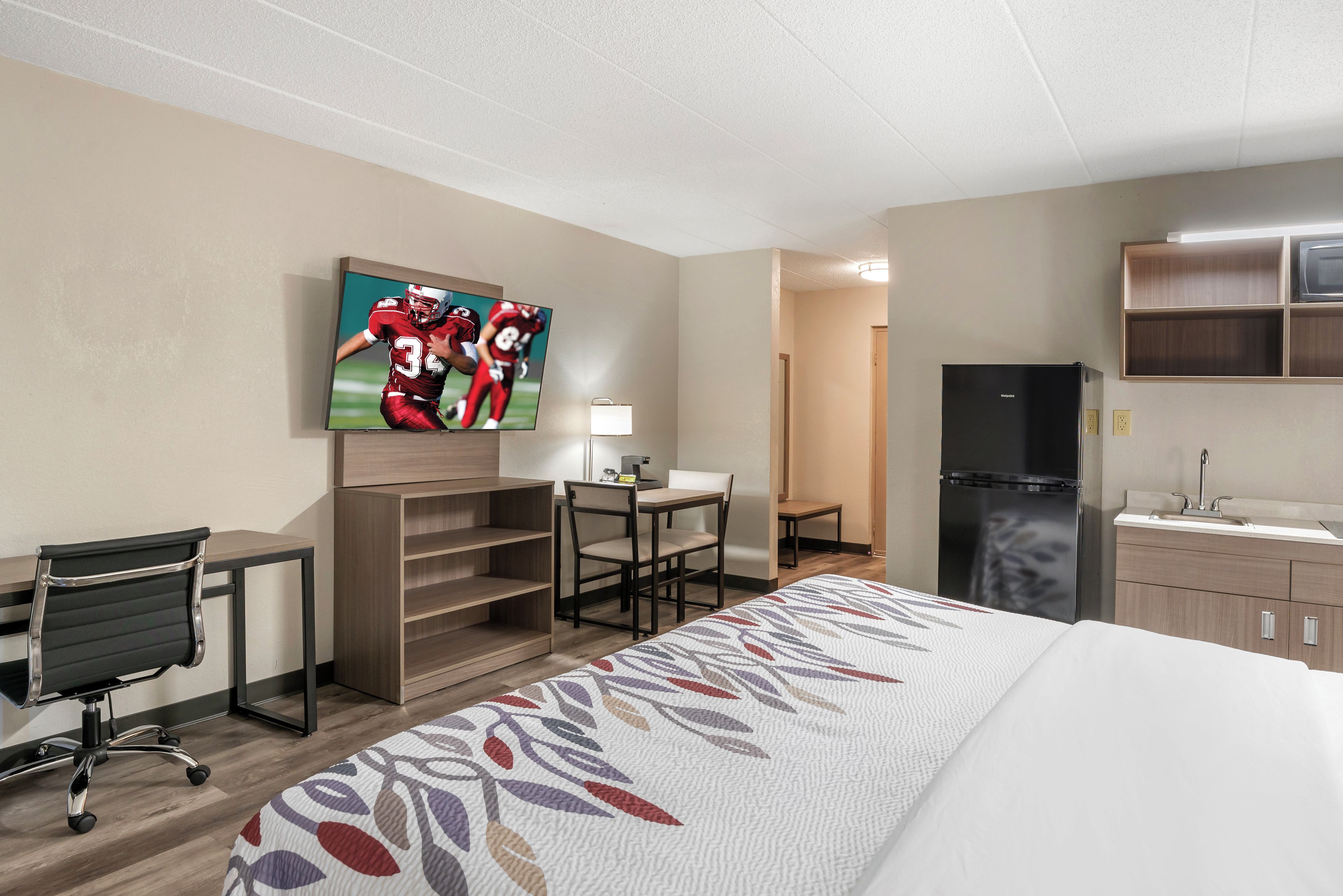 Ein Hotelzimmer mit Bett, Schreibtisch, Stuhl, Fernseher und Küchenzeile.