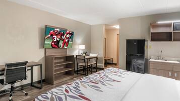 Ein Hotelzimmer mit Bett, Schreibtisch, Stuhl, Fernseher und Küchenzeile.