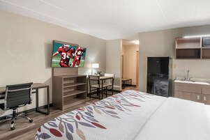 Ein Hotelzimmer mit Bett, Schreibtisch, Stuhl, Fernseher und Küchenzeile.