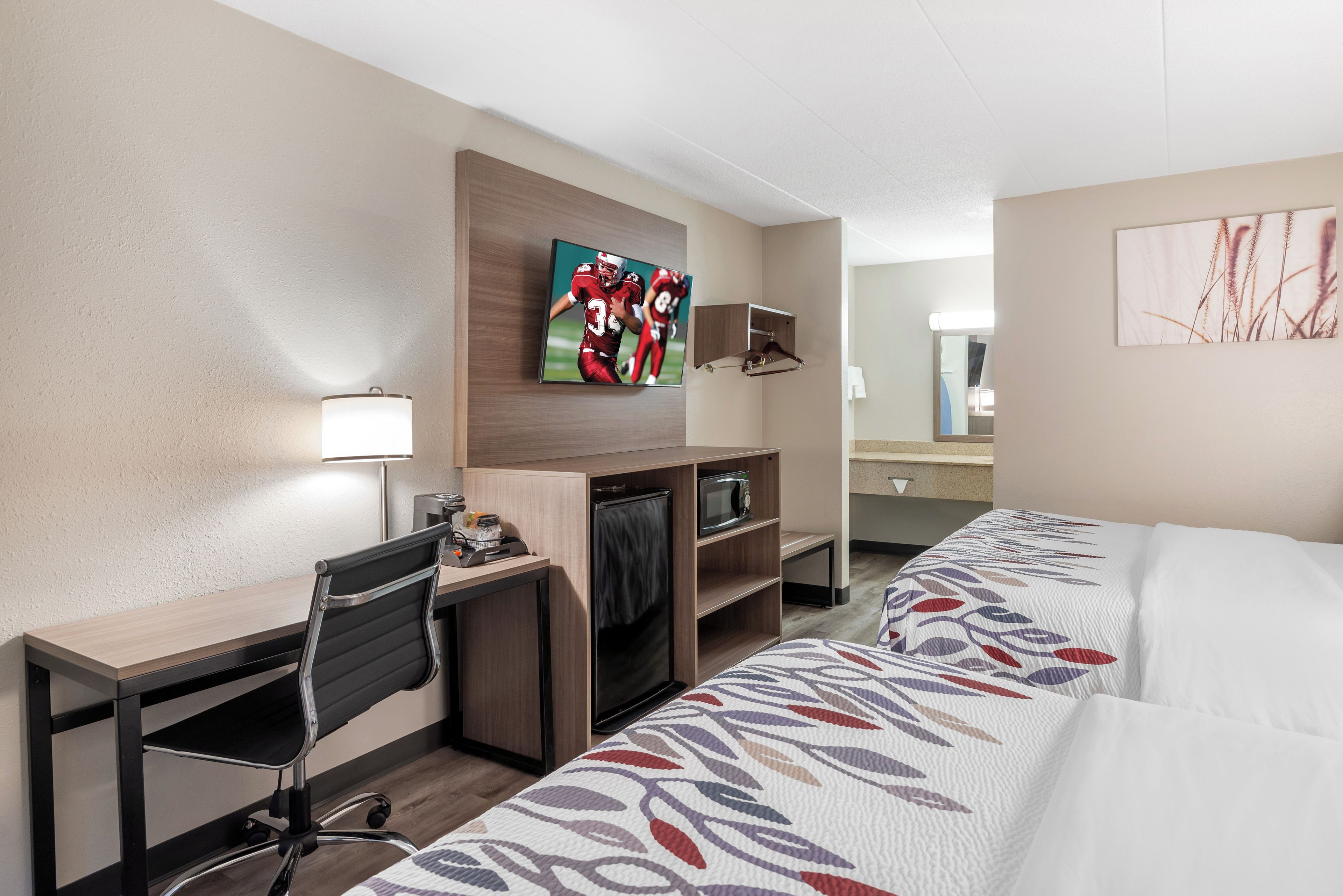 Une chambre d’hôtel équipée d’un bureau, d’une télévision, d’un four à micro-ondes, d’une chaise et d’un lit avec une couvre-lit à motifs.
