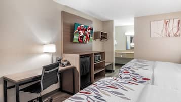 Une chambre d’hôtel équipée d’un bureau, d’une télévision, d’un four à micro-ondes, d’une chaise et d’un lit avec une couvre-lit à motifs.