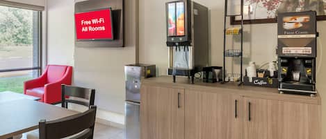 A modern kitchenette with a coffee machine, a refrigerator, a TV displaying 'Free Wi-Fi All Rooms,' and a red chair.