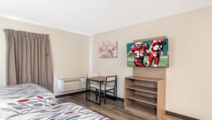 Une chambre d’hôtel avec un lit, un bureau, une chaise, une télévision et une étagère.