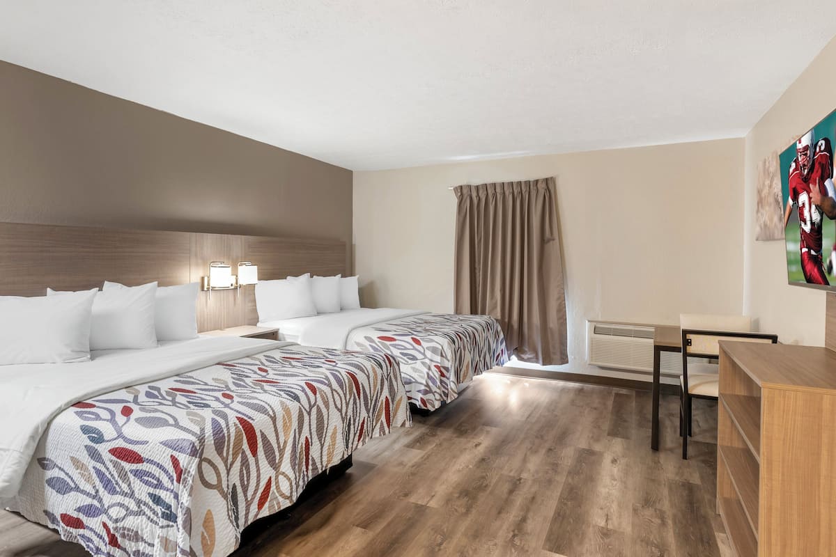 Een hotelkamer met twee bedden, een bureau, een stoel en een raam met gordijnen.