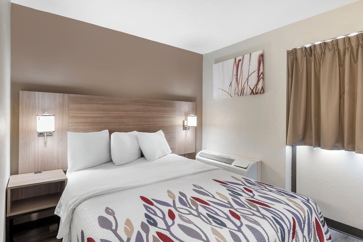 Een hotelkamer met een bed, nachtkastjes, een wandairconditioner en een raam met gordijnen.