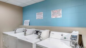 Une buanderie équipée de plusieurs machines à laver et de plusieurs séchoirs, des panneaux indiquant que l’hôtel n’est pas responsable des objets perdus ou volés, et des instructions d’utilisation des machines à laver.