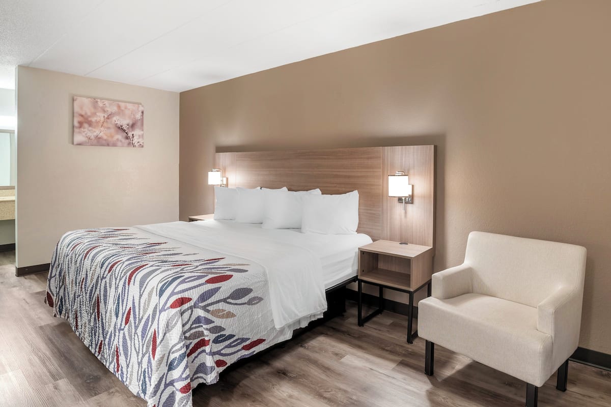 Hotelkamer met een groot bed, twee nachtkastjes, een stoel, een houten hoofdbord en een kunstwerk aan de muur.