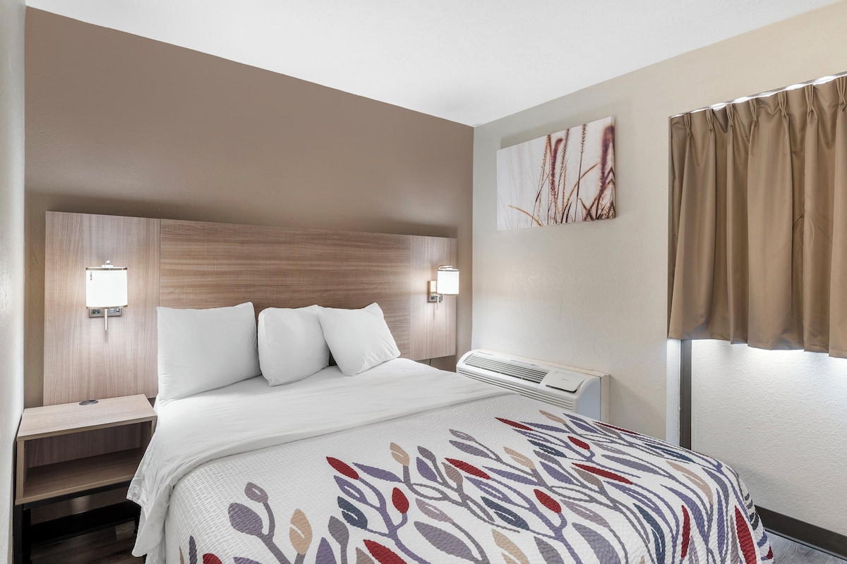 Une chambre d’hôtel avec un lit, des tables de chevet, un climatiseur fixé au mur et une fenêtre avec des rideaux.