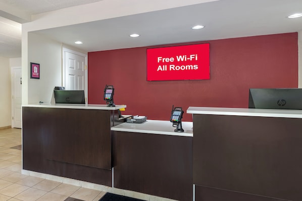 Zona de recepción de un hotel con una pared roja y un cartel que dice 'Wi-Fi gratis en todas las habitaciones'.