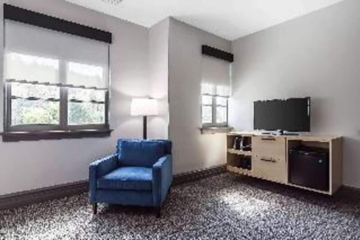 A room with a blue armchair, a television on a wooden stand, and a window with blinds.