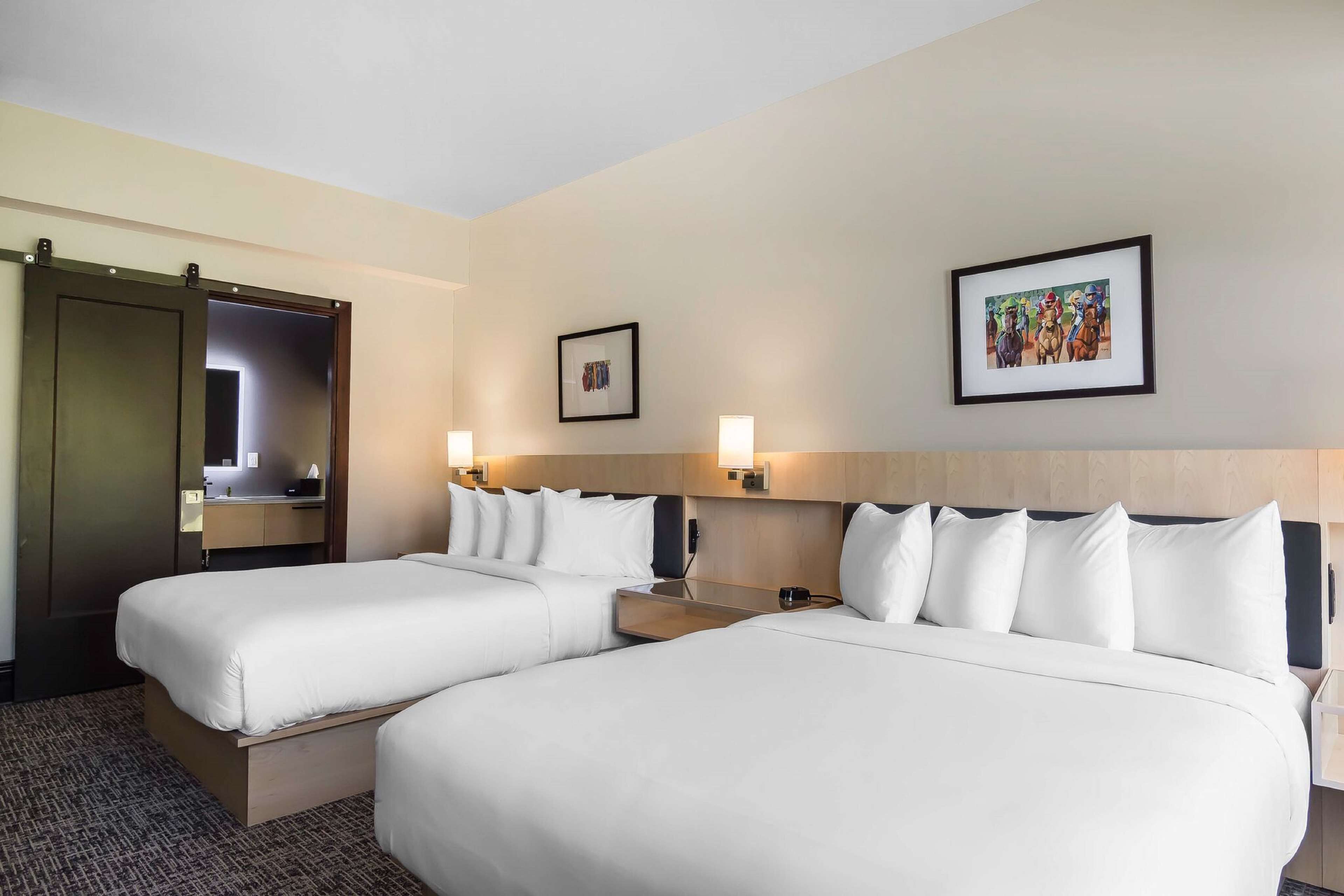 A hotel room with two beds, a wooden headboard, a nightstand, a mirror, and two wall-mounted lights.