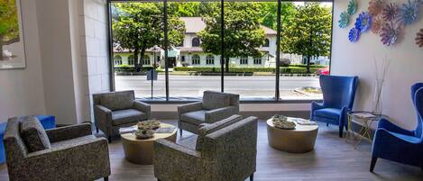 A modern lobby with multiple seating areas, large windows offering a view of the street and buildings outside.