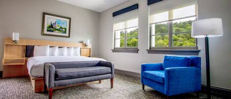 Una habitación de hotel con una cama, un sillón azul, una mesita de noche, una lámpara y un cuadro en la pared.