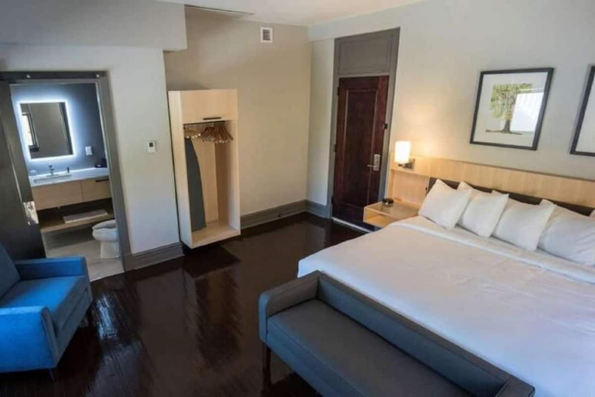 A hotel room with a bed, a seating area, a mirror, a wardrobe, and a nightstand.