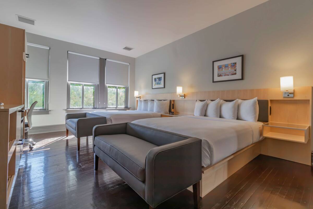A hotel room with two beds, a sofa, a desk, and a window with blinds.