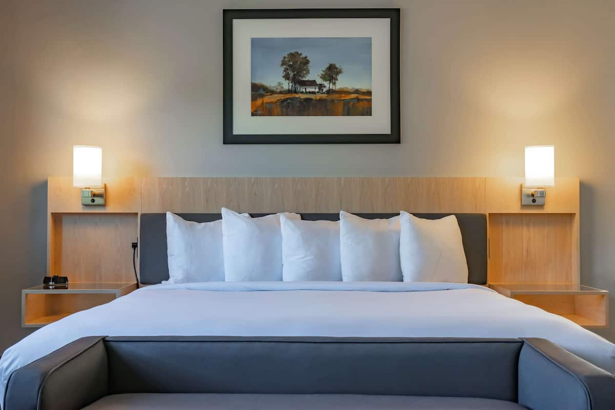 A neatly made bed with white linens, a headboard with a light wood finish, and two bedside tables with wall-mounted lamps.