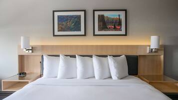 Una habitación de hotel con una cama grande, dos lámparas de pared y dos cuadros enmarcados sobre la cama.