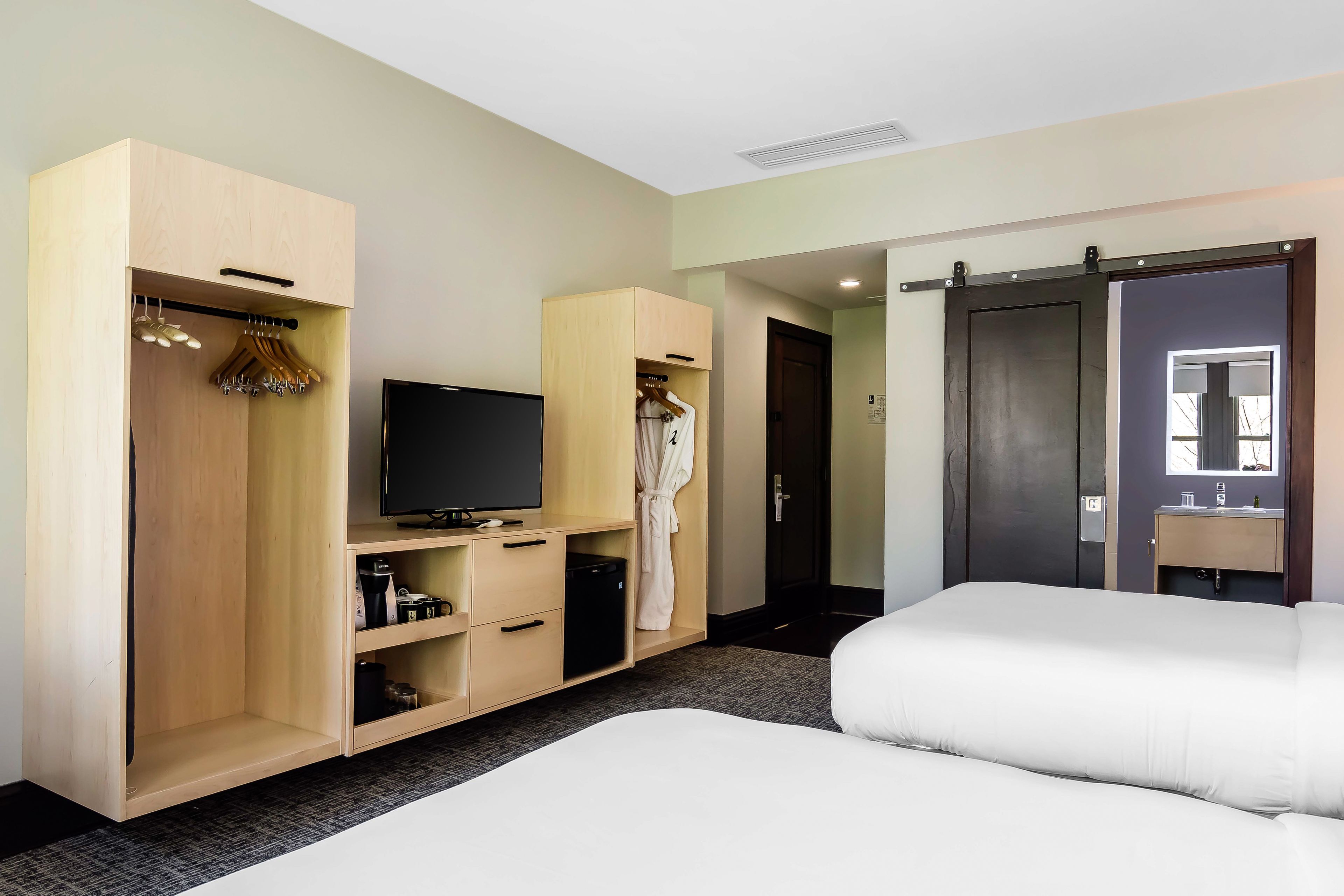 Habitación de hotel con cama, televisión, armario y baño con espejo.