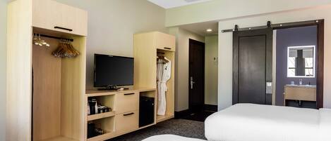Habitación de hotel con cama, televisión, armario y baño con espejo.