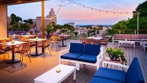 An outdoor patio with wicker furniture, white tables, and blue cushions. There are string lights and potted plants. - The Waters Hot Springs, Tapestry Collection by Hilton (Hot Springs)