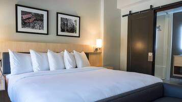 Une chambre d’hôtel comprenant un lit, des tables de chevet, des lampes fixées au mur et une porte coulissante donnant accès à la salle de bain.