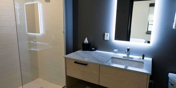 Un bagno moderno con cabina doccia in vetro, un lavandino bianco con specchio sopra e il water a destra.