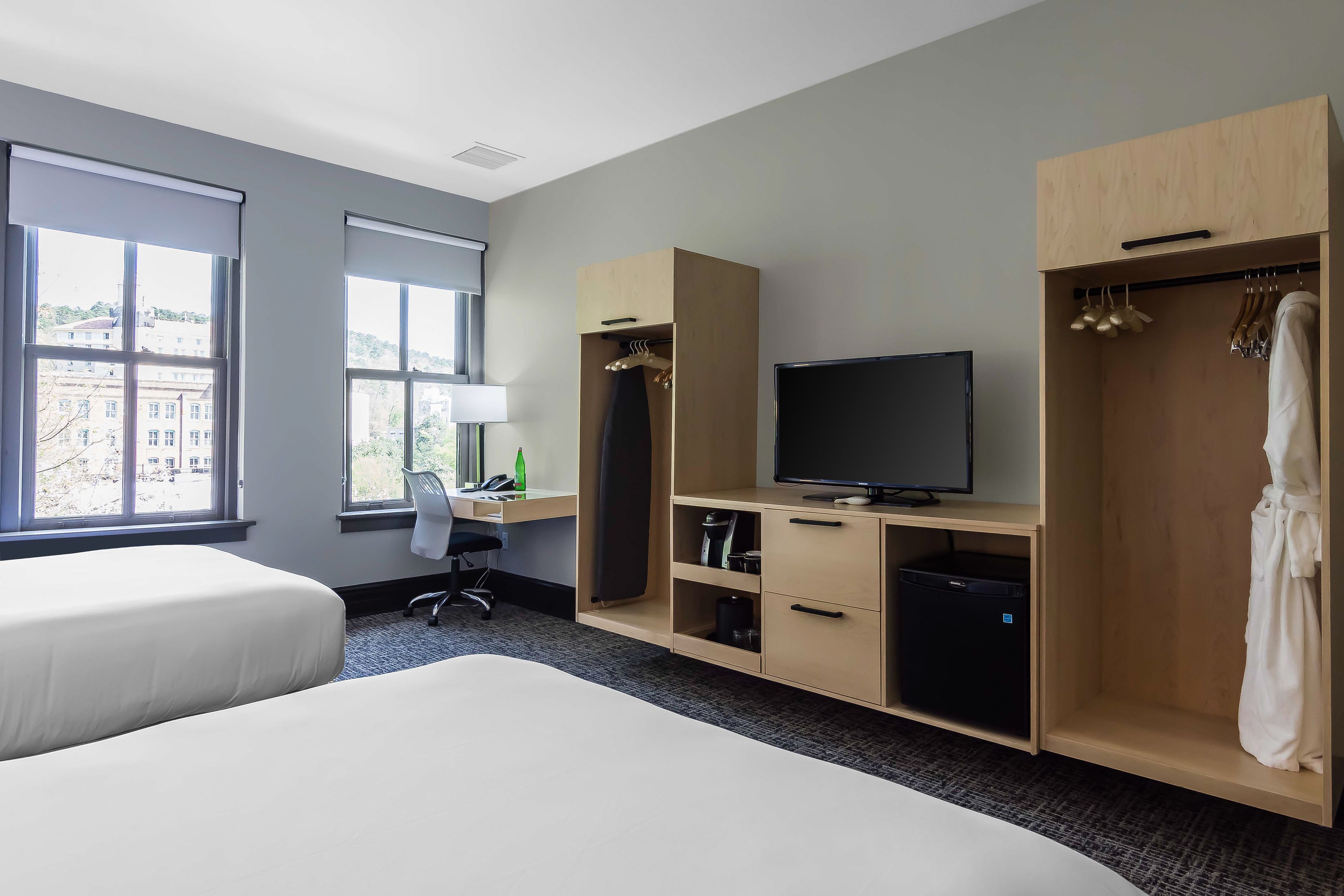 A hotel room with two beds, a desk with a computer, a TV, and a wardrobe.