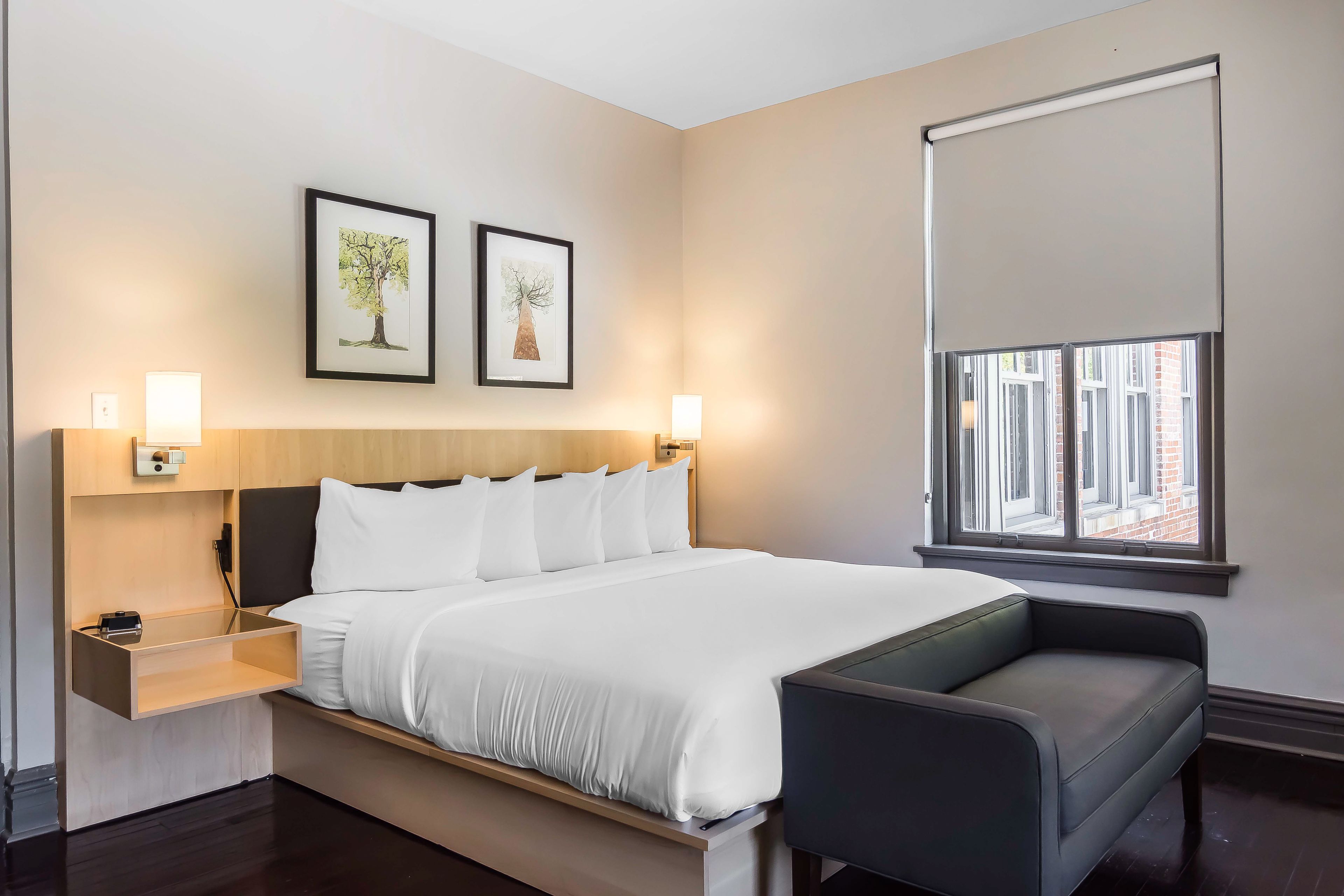 Een moderne hotelkamer met een groot bed, nachtkastjes, een bureau en een raam met jaloezieën.