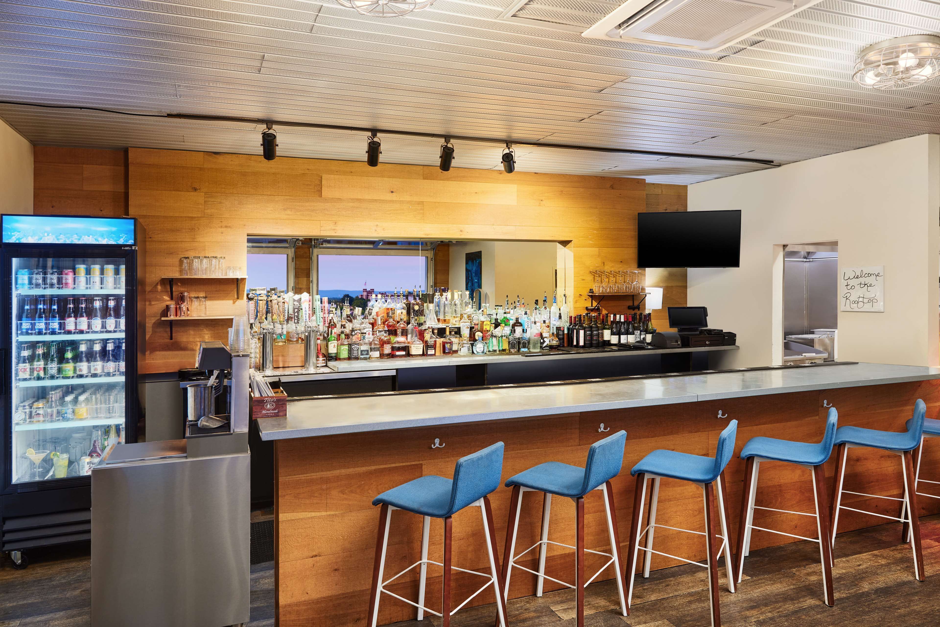 A bar area with a long counter, bar stools, a beverage dispenser, and a television mounted on the wall.
