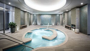 A modern indoor pool with a circular design, surrounded by a tiled floor and walls with mosaic tiles.