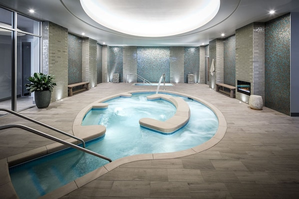 A modern indoor pool with a circular design, surrounded by a tiled floor and walls with mosaic tiles. - Lodge Kohler (Green Bay)