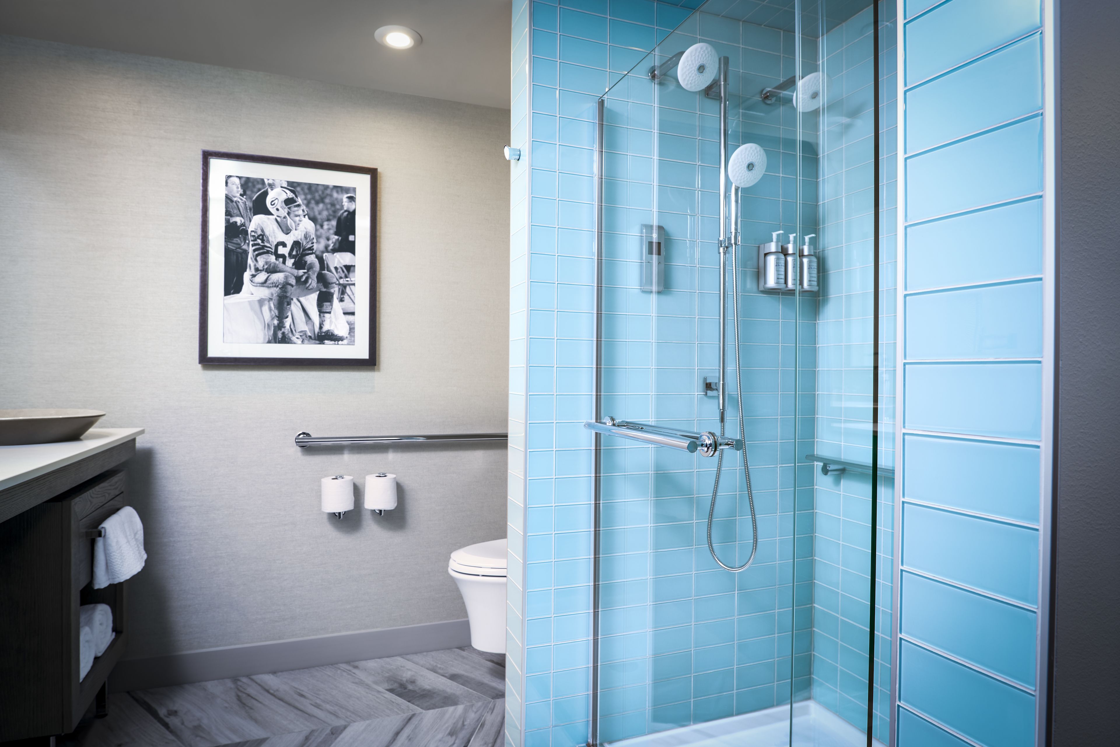 A bathroom with a glass-enclosed shower, a sink with a mirror, and a framed photograph on the wall.