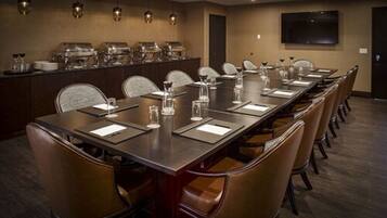 Un salón de conferencias con una larga mesa, sillas, un mostrador de buffet y una televisión montada en la pared.