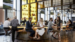A spacious bar area with high ceilings and large windows, featuring a variety of seating options and a well-stocked bar counter.