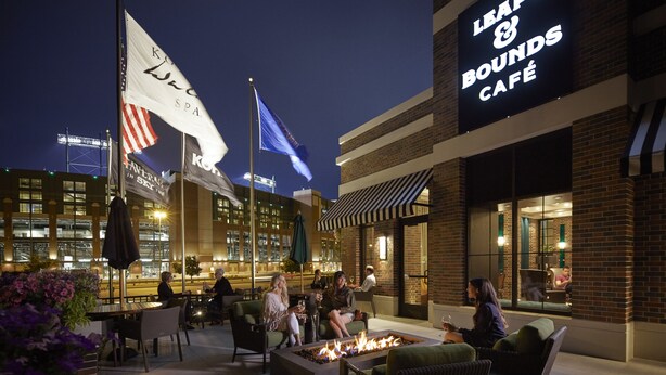 An outdoor seating area with a fire pit, tables, and chairs, in front of a building with a sign for 'Leaps & Bounds Café'.