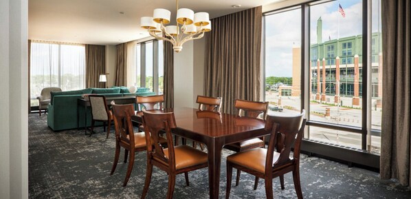 A hotel room with a dining table, chairs, a sofa, and a large window with a view of a building. - Lodge Kohler (Green Bay)