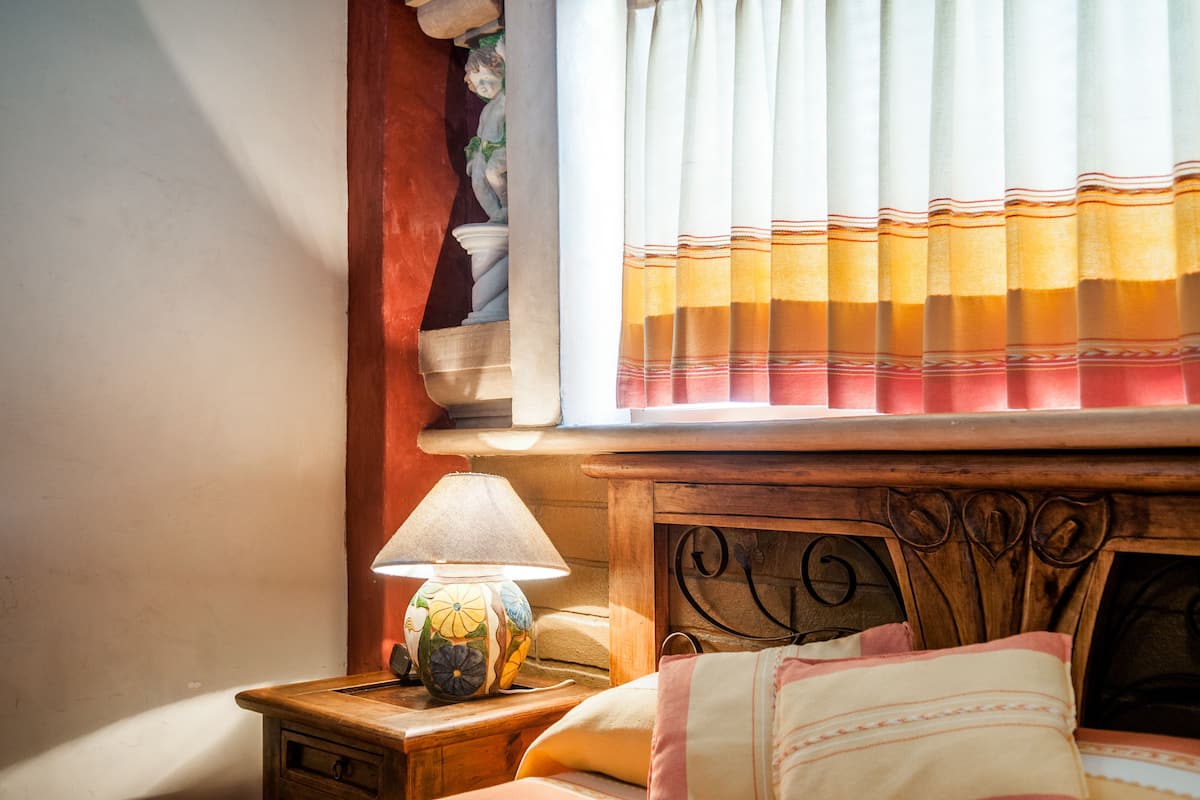 Quarto com cabeceira de madeira, abajur e janela com cortinas.