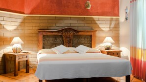 A neatly made bed with a white bedspread and pillows, a wooden headboard, and two bedside tables with lamps. - Raintree`s Las Cupulas Oaxaca (San Felipe del Agua)